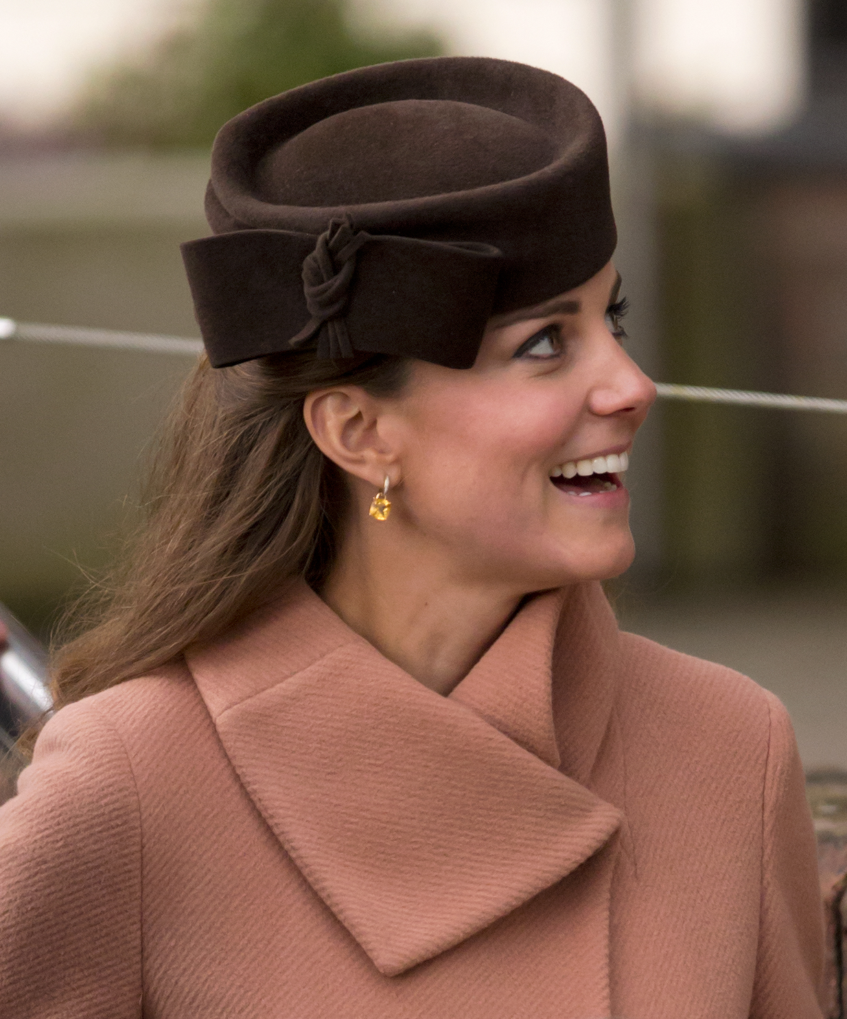 Kate Middleton wearing a mauve coat and brown hat smiling and looking to the side