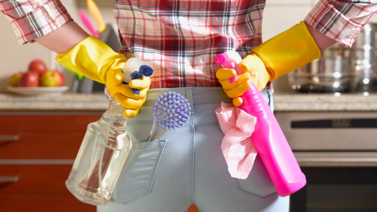 rear view of a a woman&#039;s back. she is in jeans and is holding two spray bottles of household cleaner