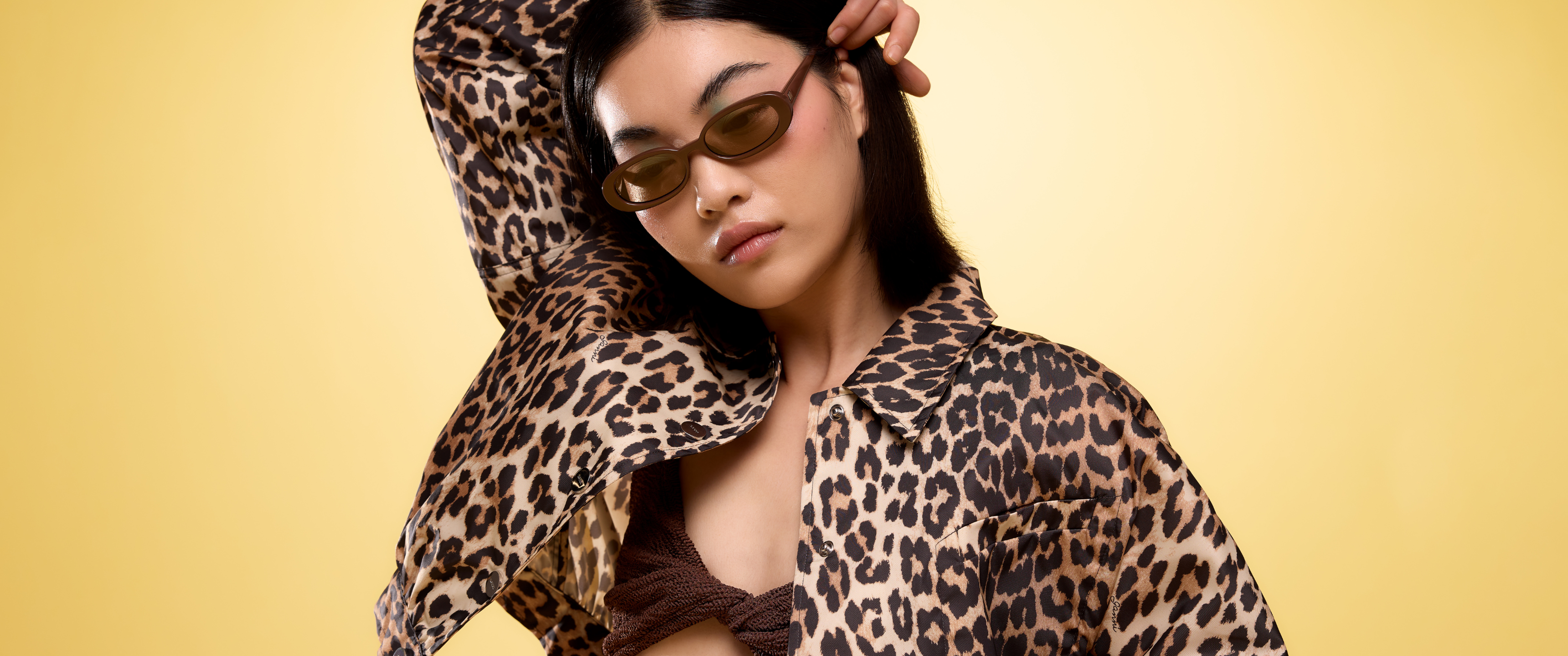 Model wearing a bralette, a leopard print shirt and brown sunglasses sold at Coggles