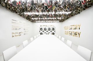The Dream Room. White boardroom table with white chairs, sneakers hanging from ceiling and machinery on wall