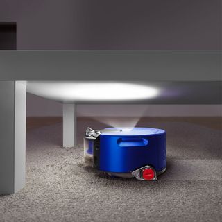 Dyson 360 Heurist robot vacuum cleaner under a bed with its light on