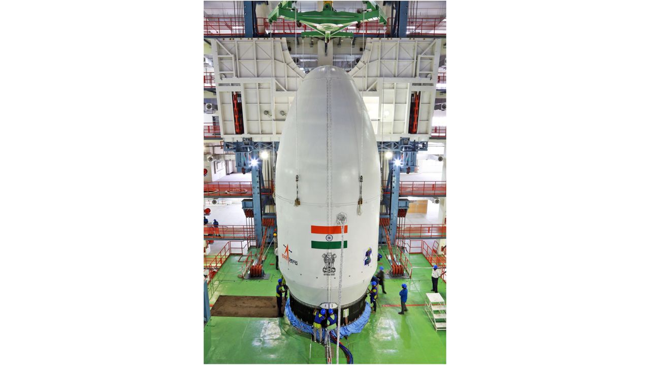 a white conical payload fairing sits atop its rocket inside a huge building