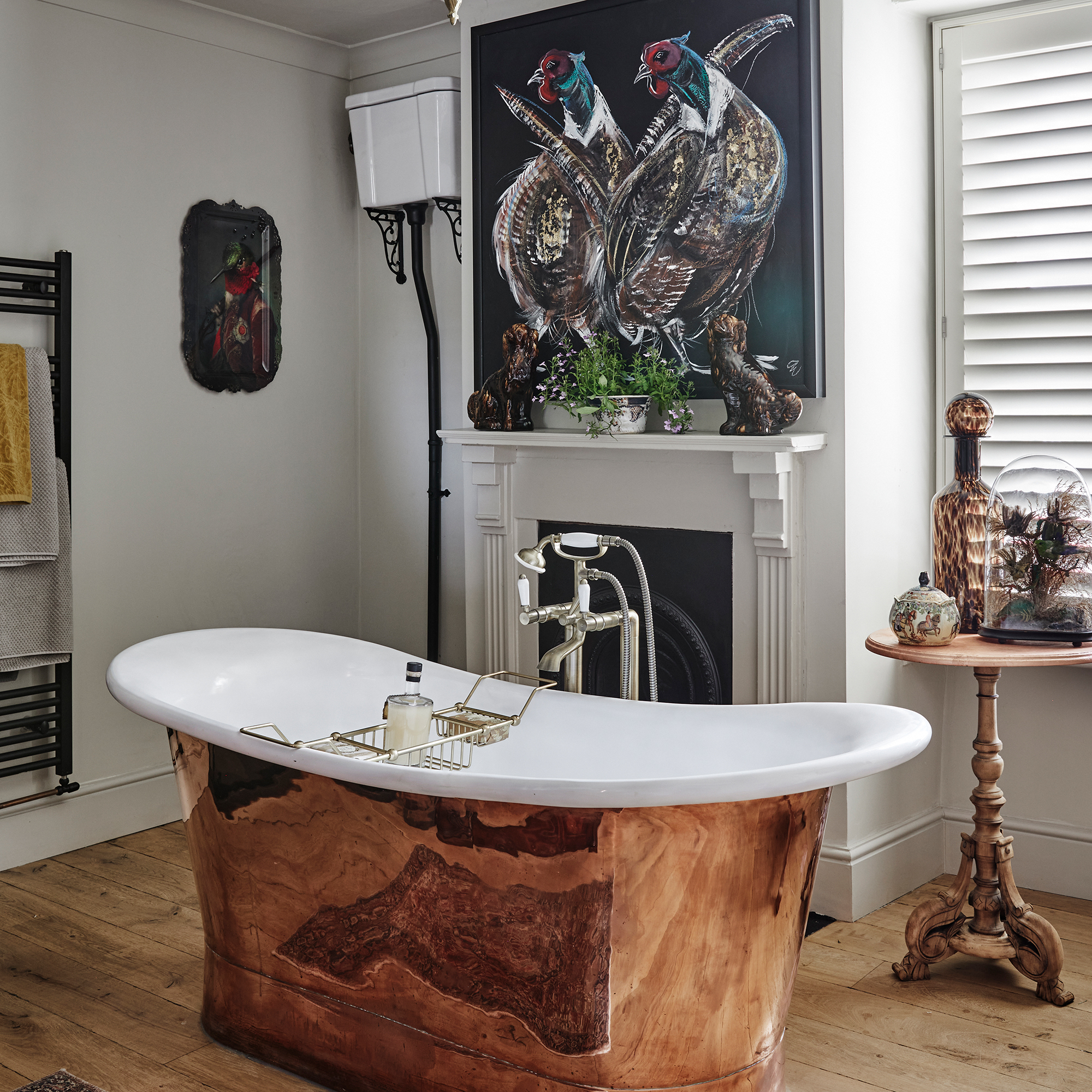 luxurious bathroom with copper freestanding bath, fireplace, artwork and wooden floor