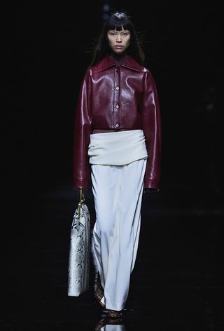 a photo showing the fall jacket trend cropped leather jackets on the Khaite runway with a model wearing a red leather jacket with a white maxi skirt, snakeskin bag, and heels