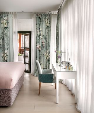 A bedroom with pale green curtains printed with large pink and white flowers