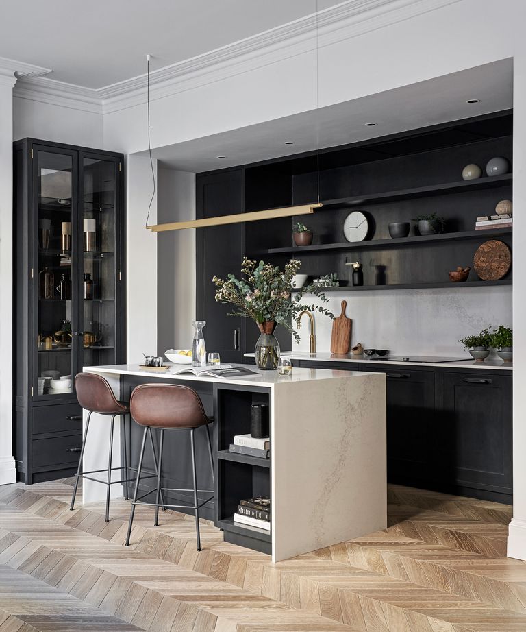 An example of small kitchen storage ideas showing a kitchen with dark cabinets and shelving and a white island with two brown leather bar stools
