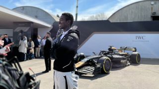 Damson Idris smiles in front of an F1 race car