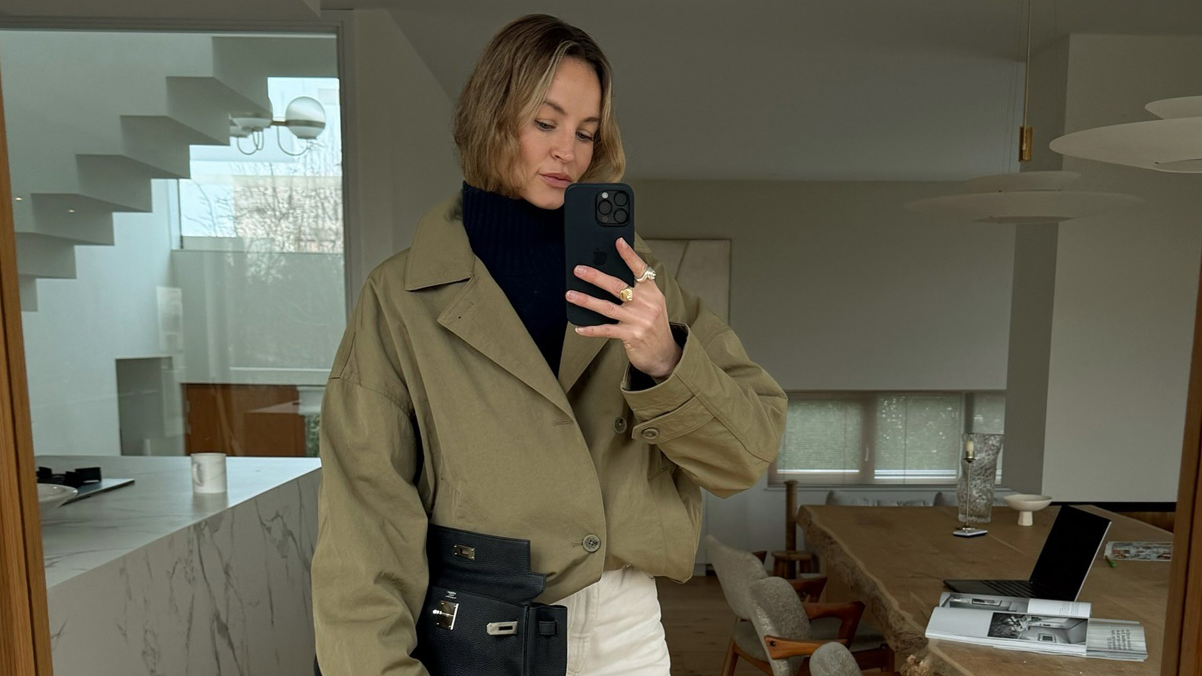 Anouk wears a black turtleneck, beige coat, and white jeans.