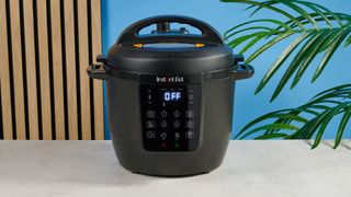 a black pressure cooker photographed against a blue background, showing its cooking presets, steam release valve, and Instant Pot branding