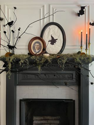 A black fireplace with a mantel decorated with moss, candles, and witch-themed artwork