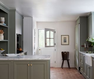 neutral shiplapped kitchen with pale green cabinets and a traditional terracotta tiled floor