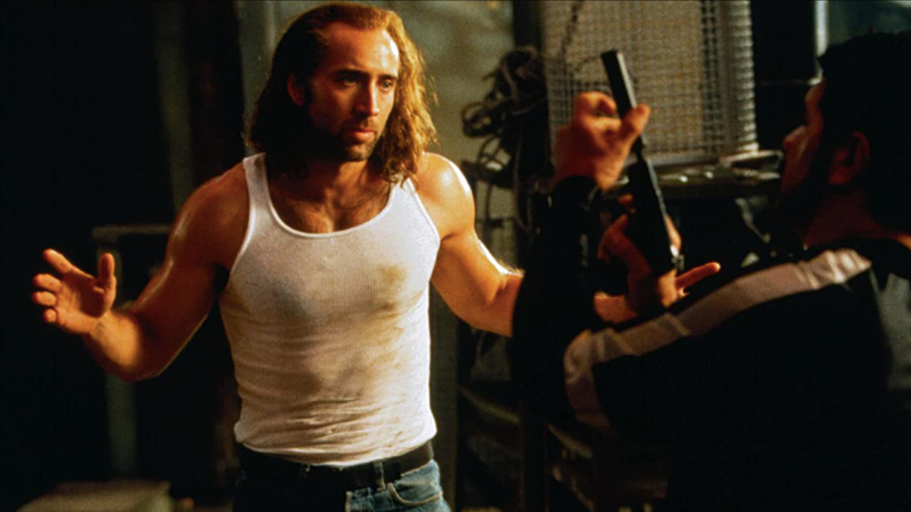 Nicolas Cage walks towards an armed man with his arms open in Con Air.