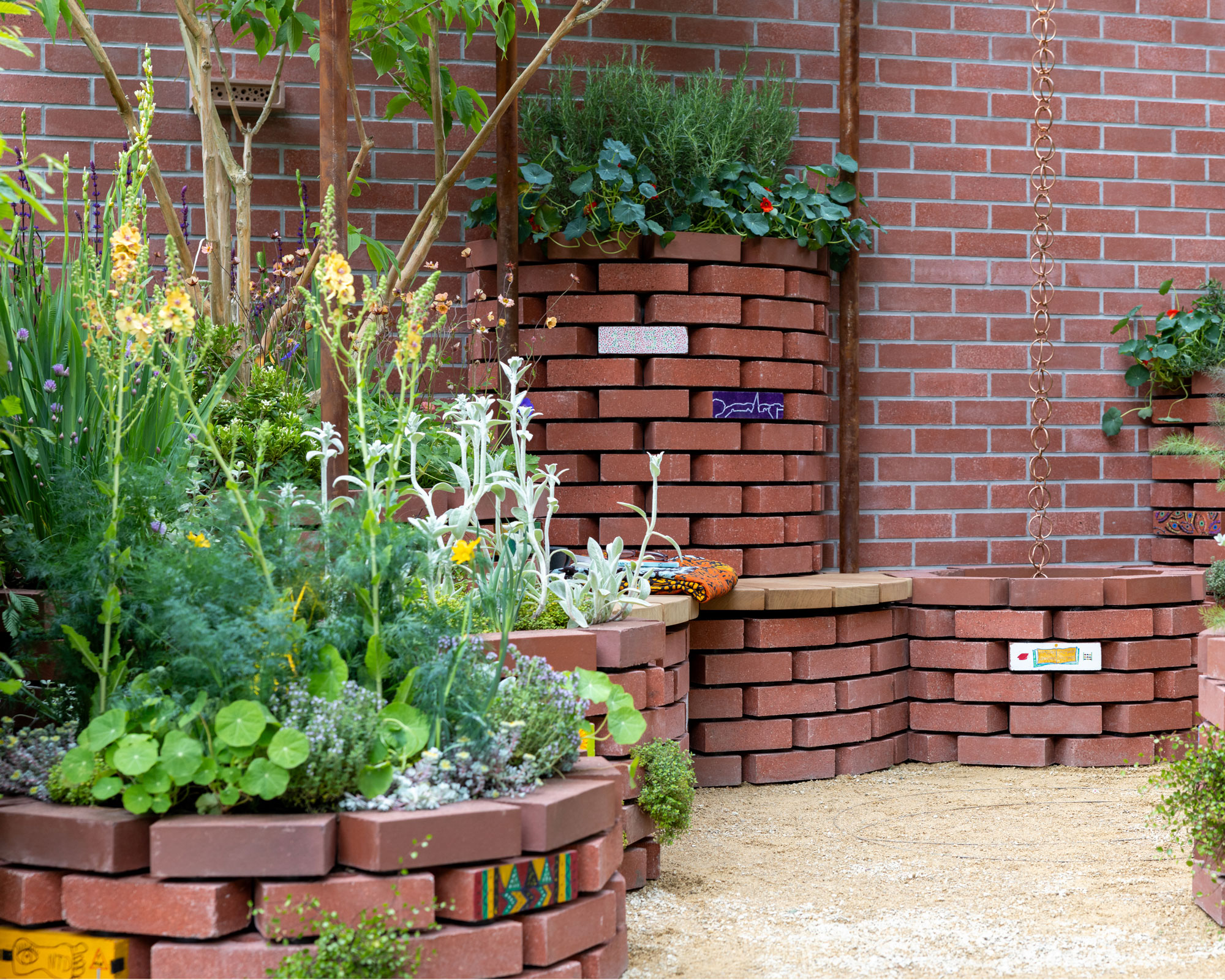 series of raised beds made of red bricks with summer planting and red brick wall behind