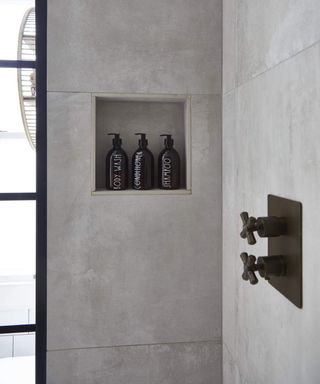 A shower shelf in grey concrete style shower with glass botttles