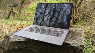 A silver MSI Creator Z17 sitting on a stone bench in a forest setting