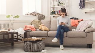 A woman sitting in a living room on her phone with mess around her