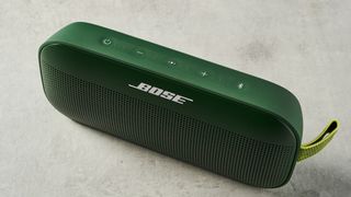 a green bluetooth speaker made by bose with a clean plastic casing and no visible woofers rests on a table