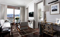 Lounge area decorated in soft, grey tones with a brown and white rug, grey furnishings and a glass coffee table