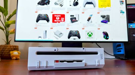 Nintendo Wii with paper eyes on front with monitor in backdrop displaying Amazon top selling gaming deals.