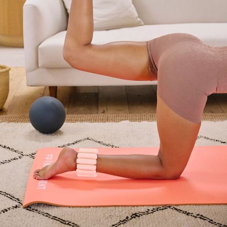 woman doing a pilates workout on coral mat wearing pink ankle weights
