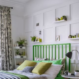 A bedroom with panelled walls adorned with floating shelves and a green bed