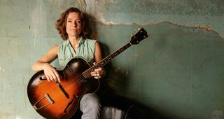 Ani DiFranco poses against a green wall with a vintage arch-top