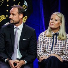 Crown Princess Mette-Marit sitting next to Crown Prince Haakon on a stage