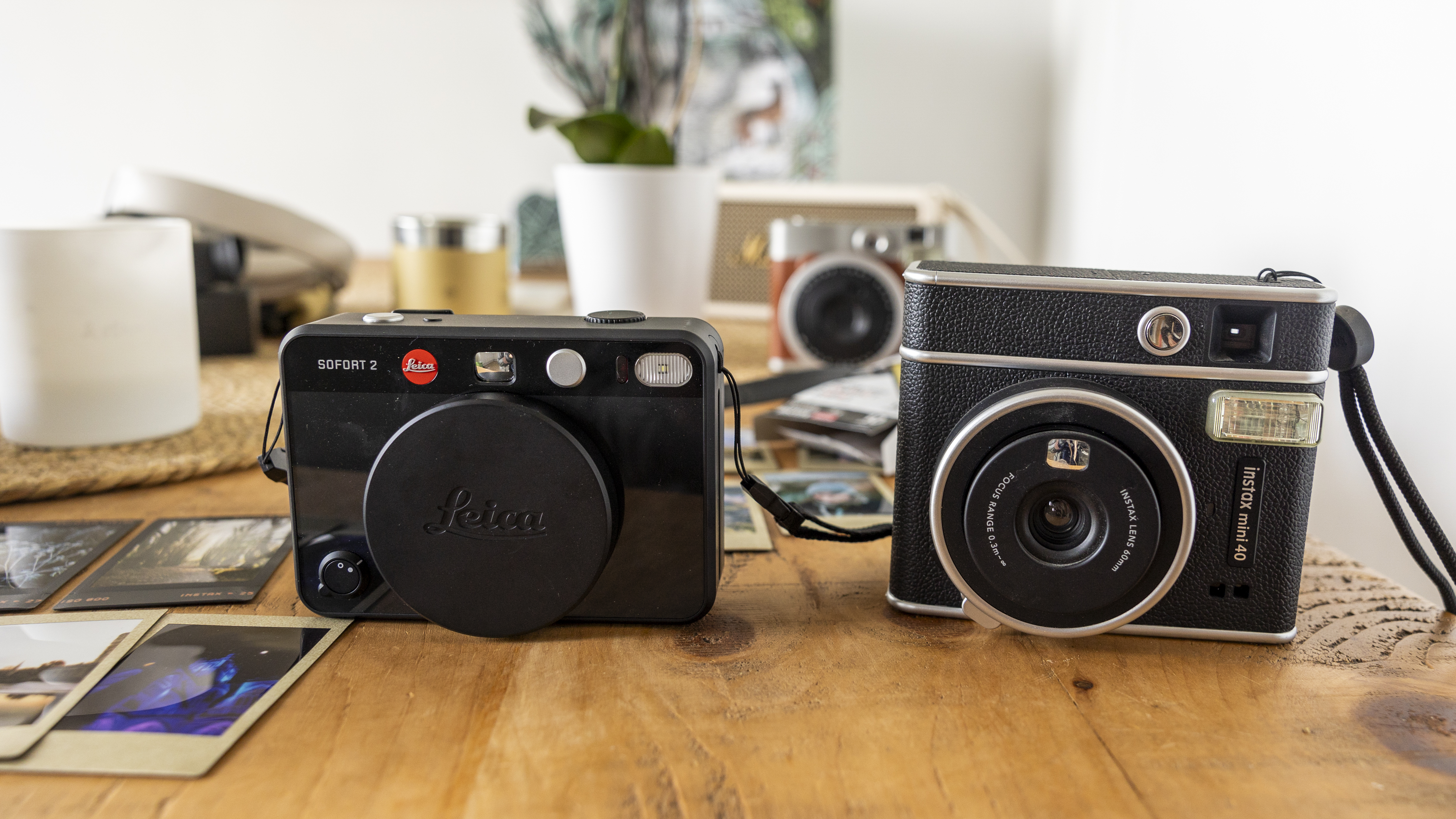 The Leica Sofort 2 on a wooden table next to the Instax Mini 90