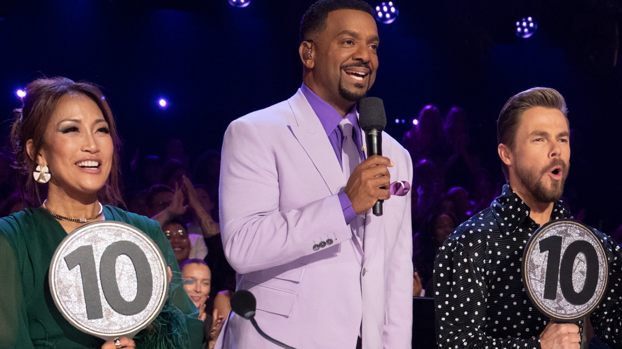 Carrie Ann and Derek hold up their "10" paddles while Alfonso stands between them in a lavender suit. 