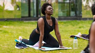 Woman doing the pigeon pose in a park on a yoga mat, one of the best yoga stretches for beginners