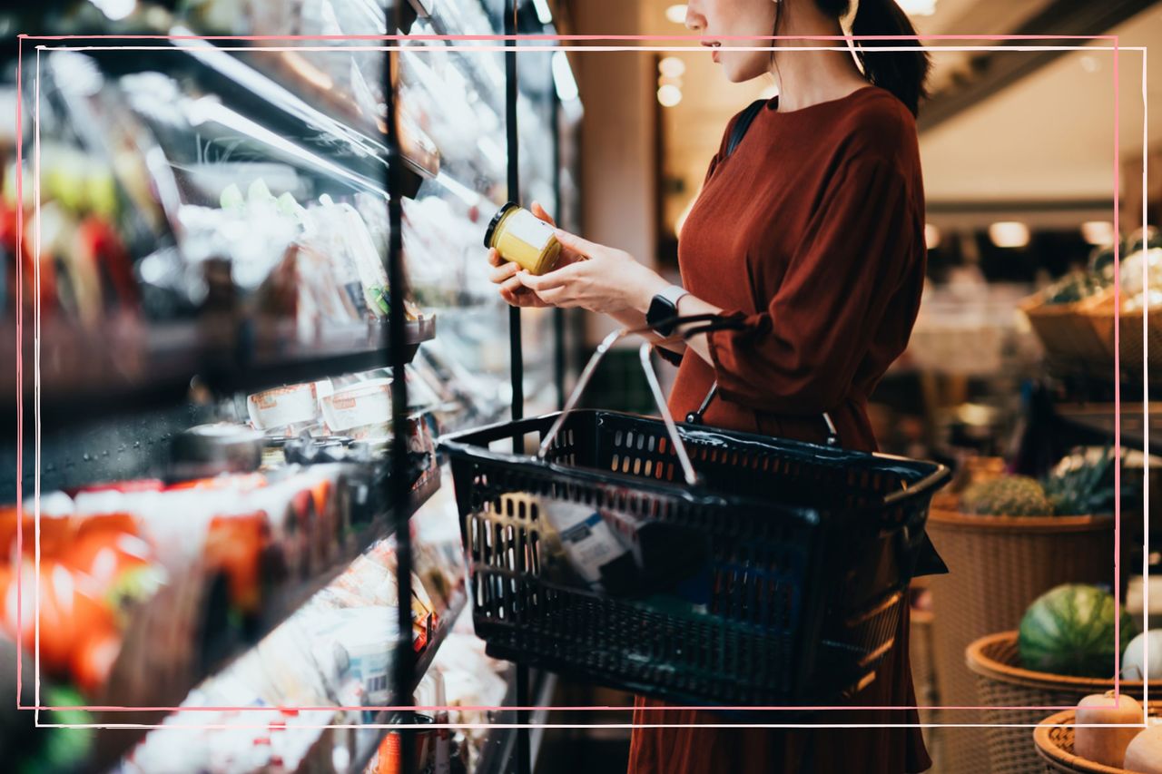 A woman carrying a shopping basket looking at the nutritional information of a product