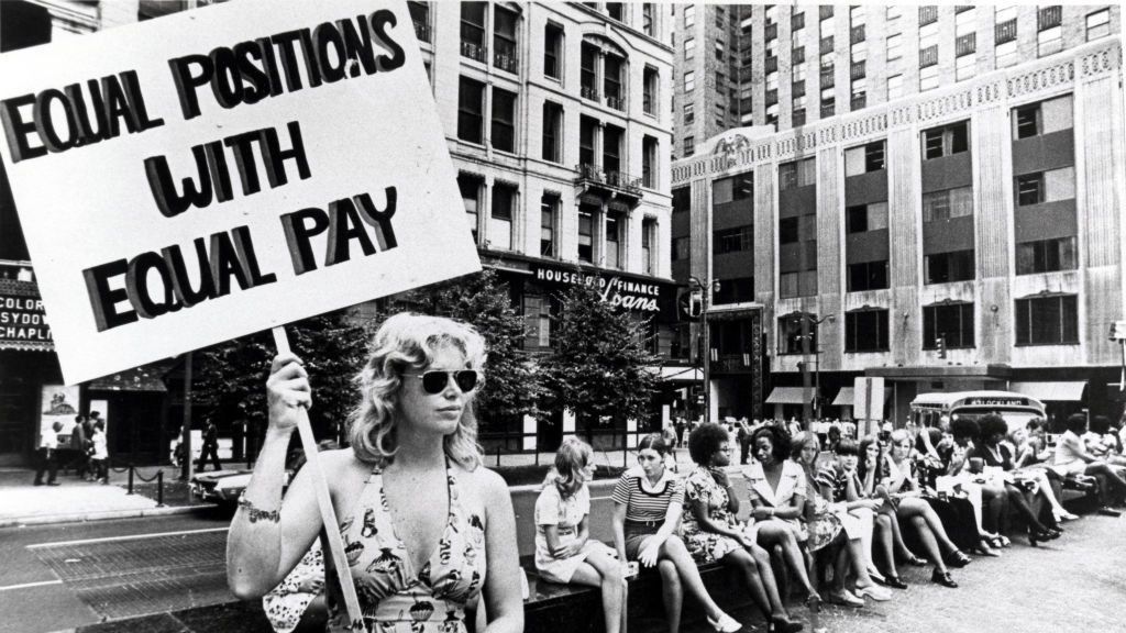 Lone woman stands on corner protesting unequal pay for women