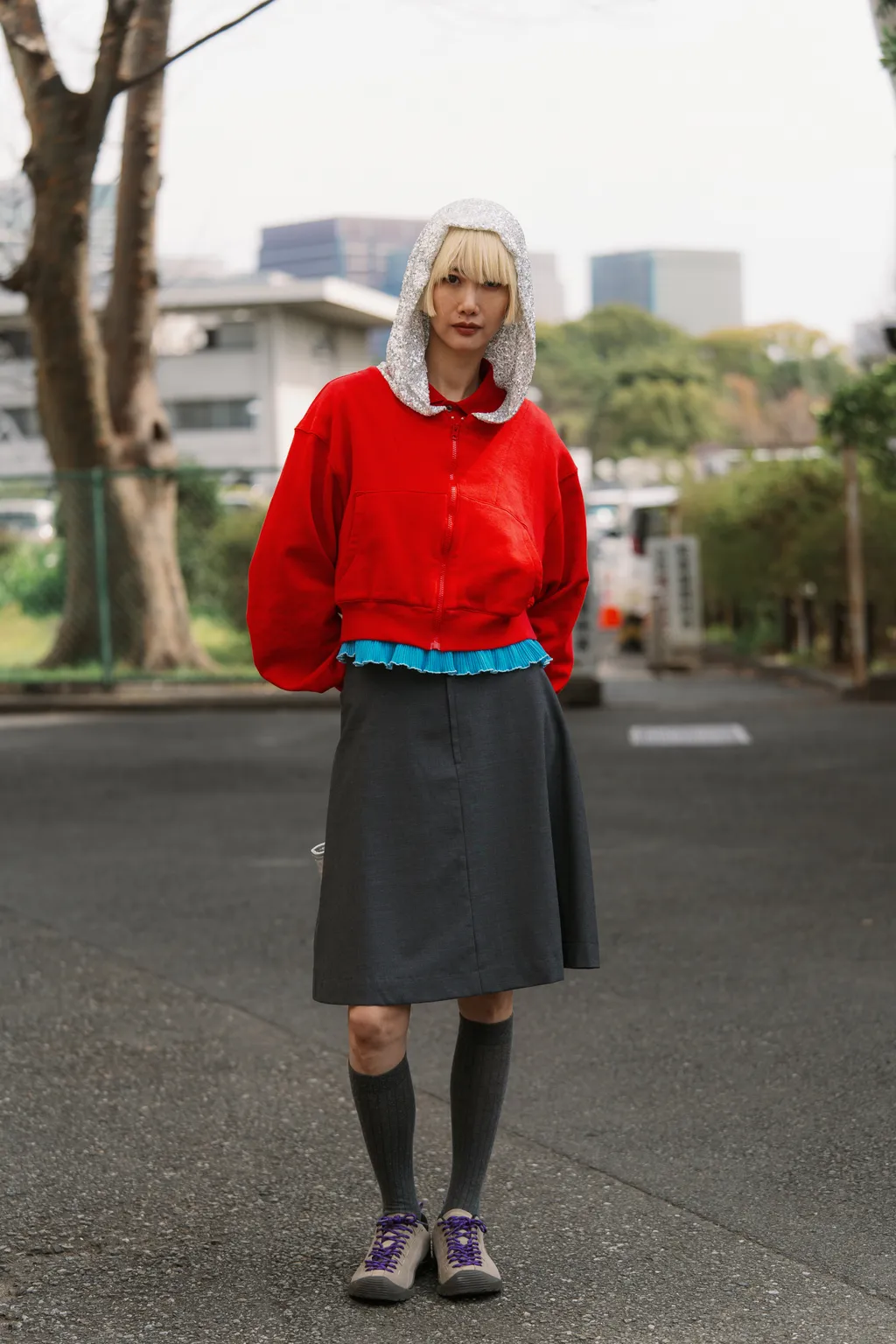 A woman wears a red sweater, gray skirt, and sneakers.