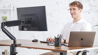 A smiling man works at a desk that has a monitor rigged up to one of the best monitor arms. 