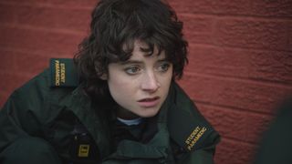 Trainee paramedic Indie Jankowski in uniform treating an unseen person against a red brick background and looking scared.