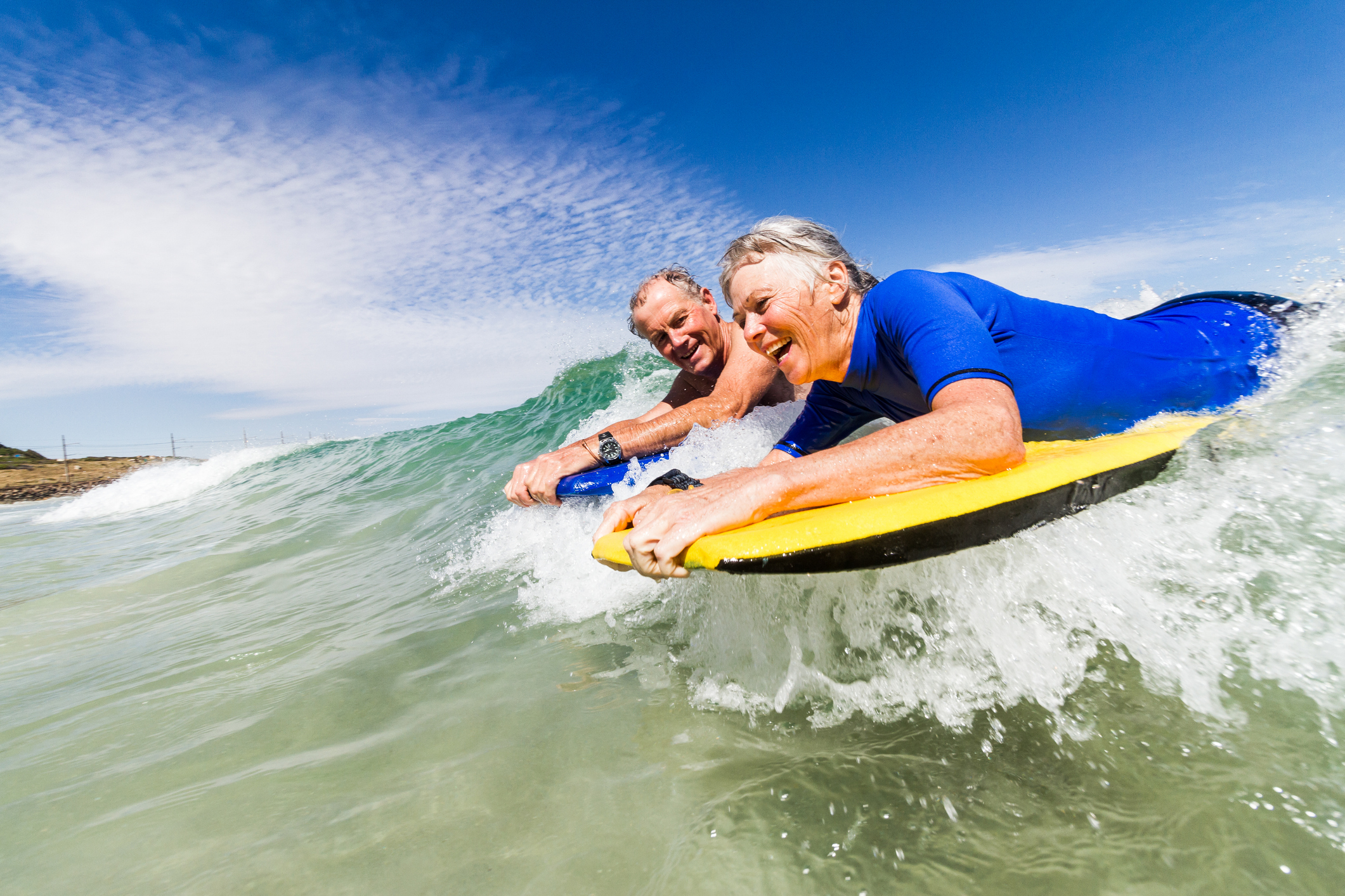 Senior couple (aged 65-69) bodyboarding together in the sea