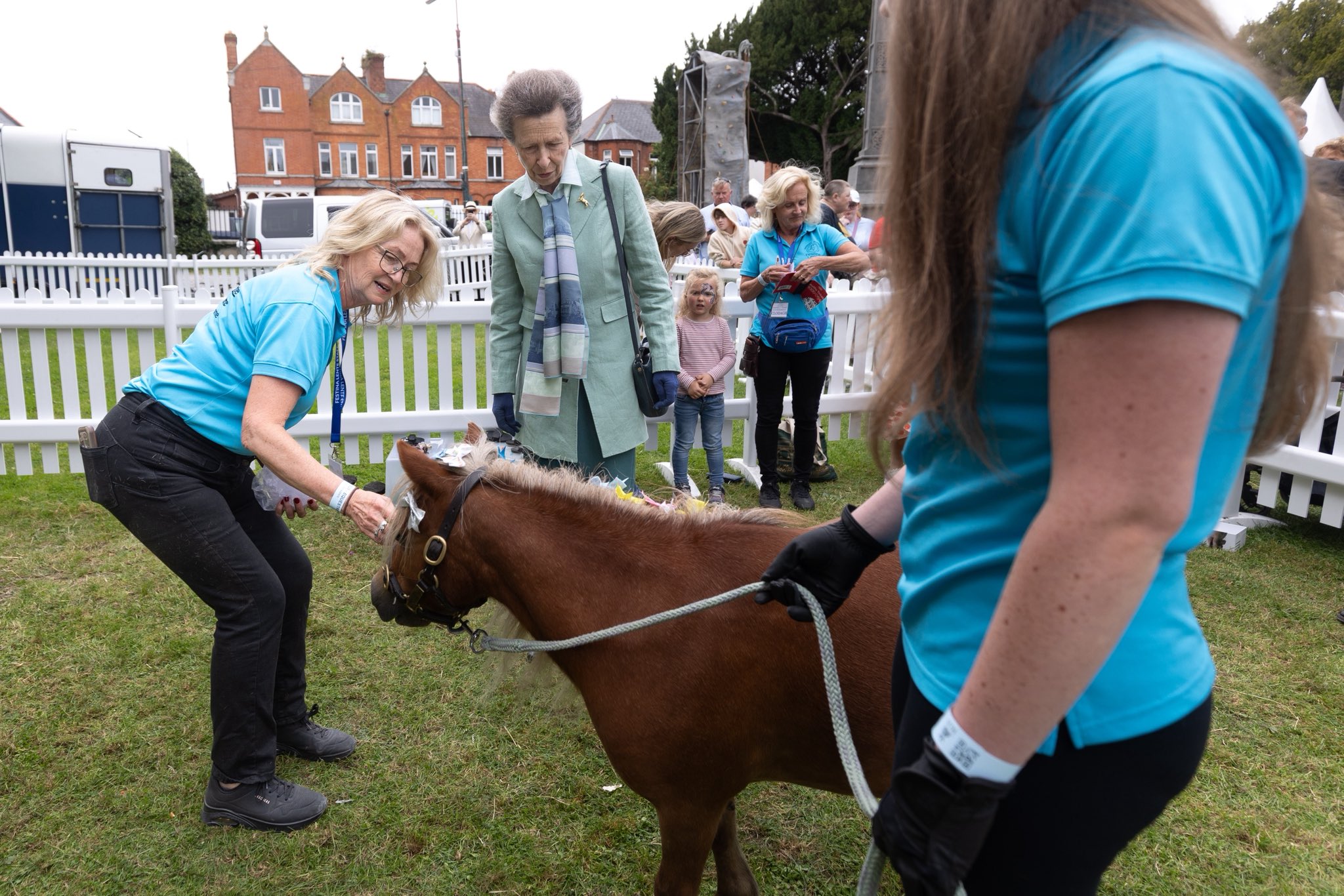 Princess Anne wearing a green blazer looking at a brown pony being held by a handler
