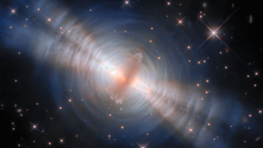An image of the egg nebula, with a glowing streak of pink gas in the middle surrounded by concentric circles of white like with four diagonal beams of light streaking from top left to bottom right all in front of a deep space starry background