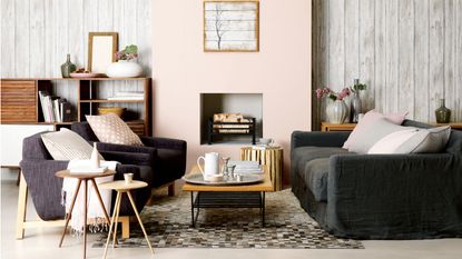 cosy living room, grey and white armchairs either side of a fireplace on a blue rug and flagstone floor. Logs filling the alcoves either side of the lit fireplace
