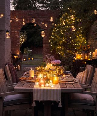 A beautifully lit table after dark with festoon lights, solar candles and lanterns