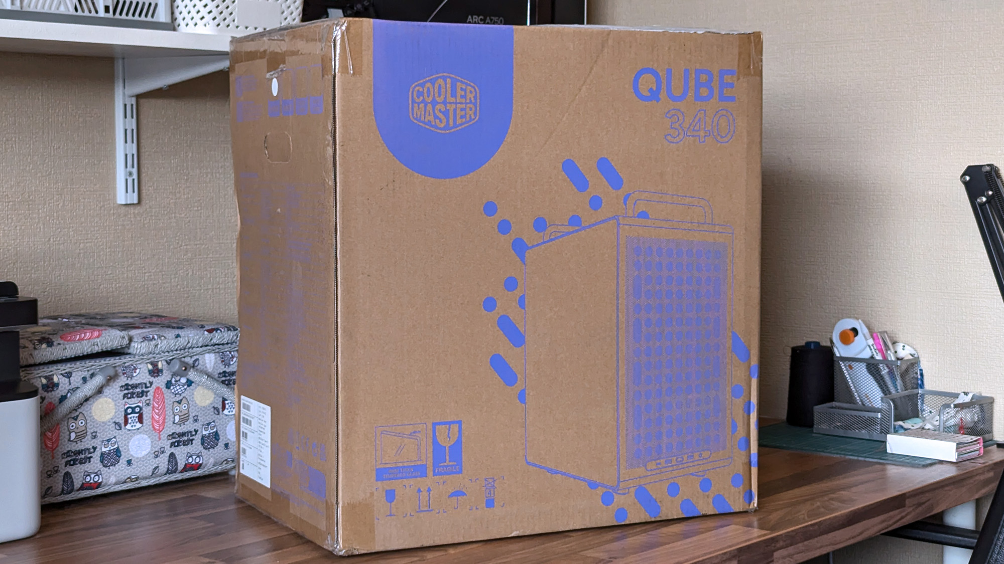 Cooler Master Qube 340 PC case in cardboard shipping box on a wooden desk