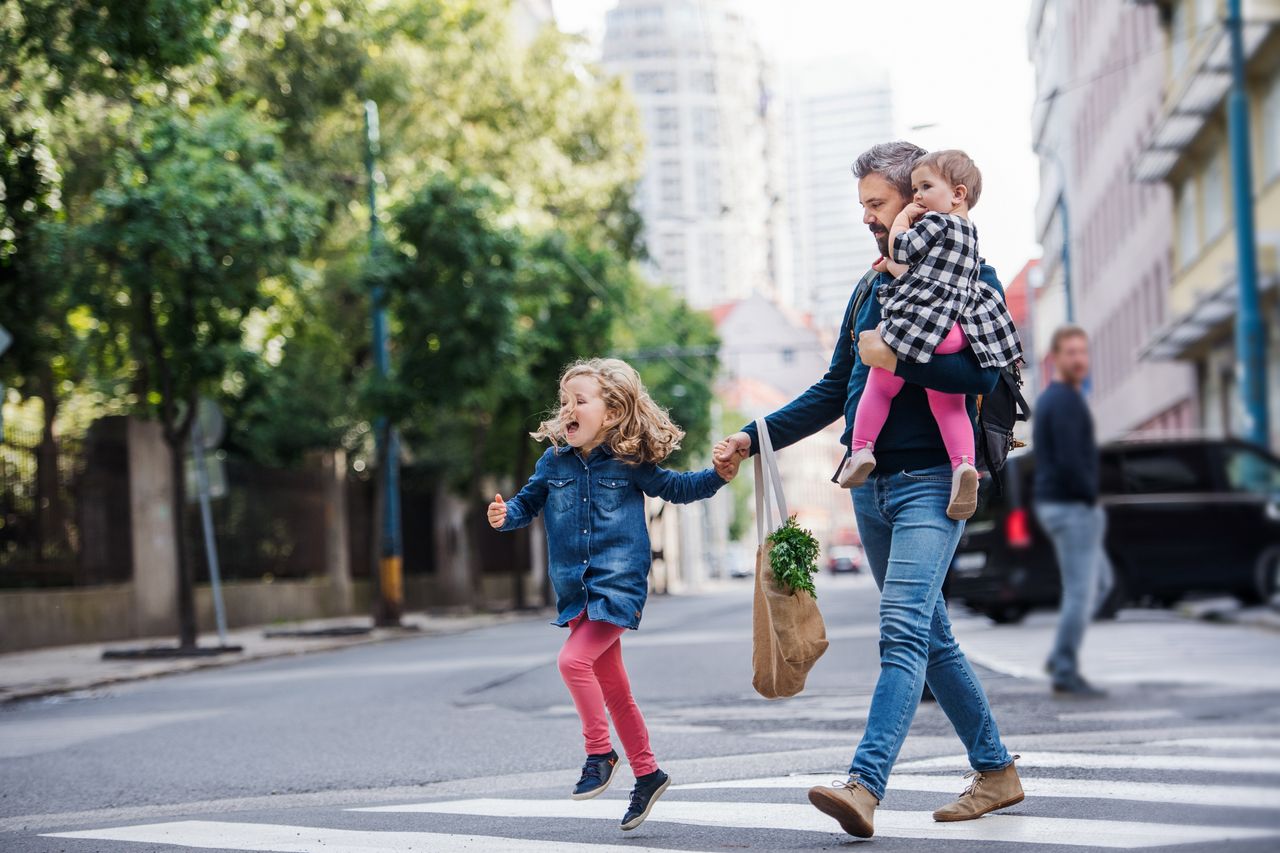 Father with small girls walking outdoors in city, crossing the road