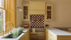 Horseshoe layout kitchen with yellow Shaker cabinets, brass hardware, red and white checkerboard backsplash, farmhouse sink, and built-in banquette seating.