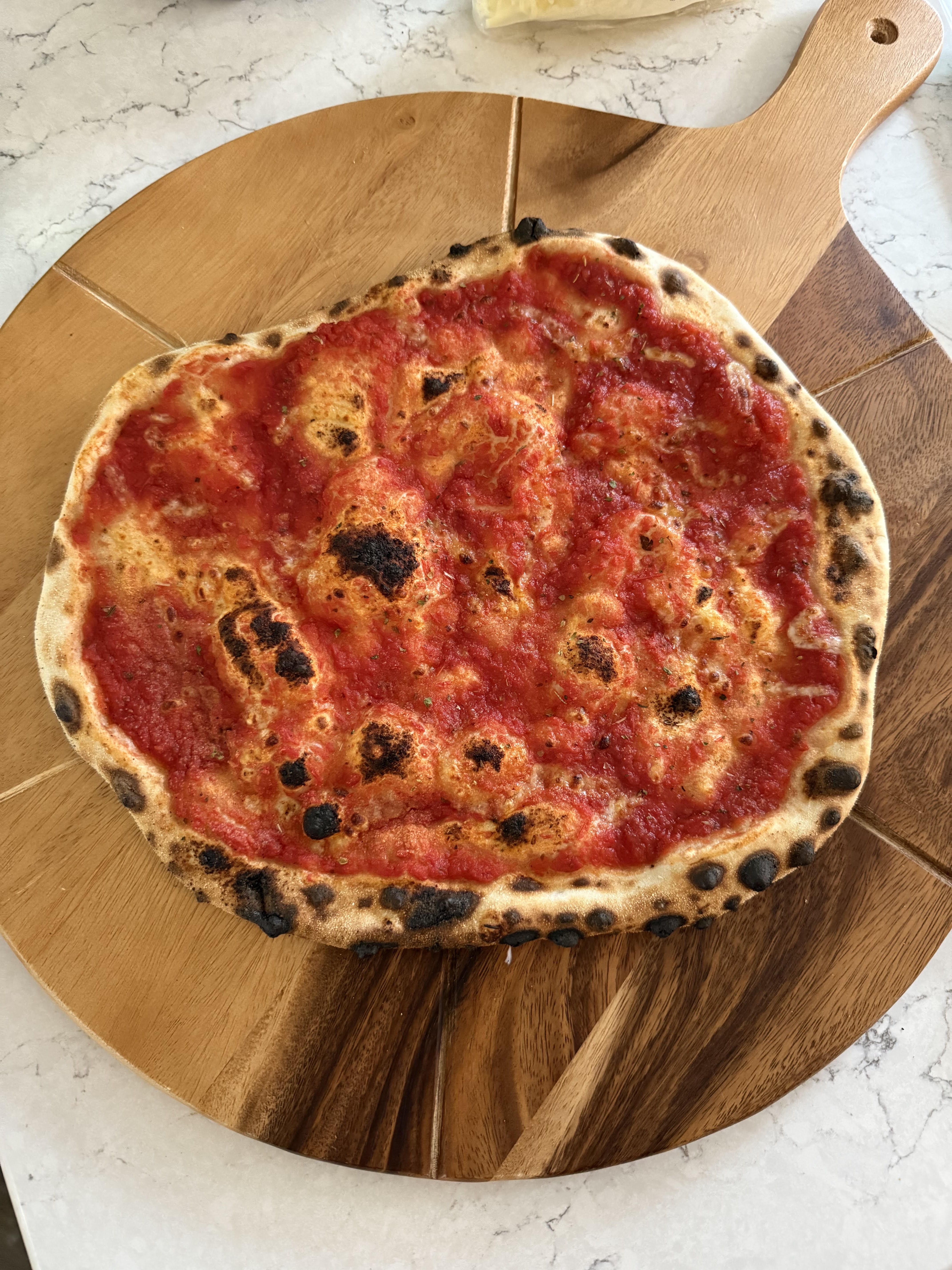 a margherita pizza on a large circular chopping board with cutting grooves on a quartz countertop