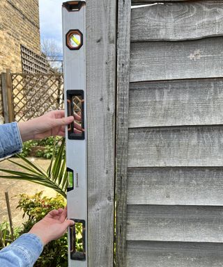 A person using spirit level to measure fence in backyard