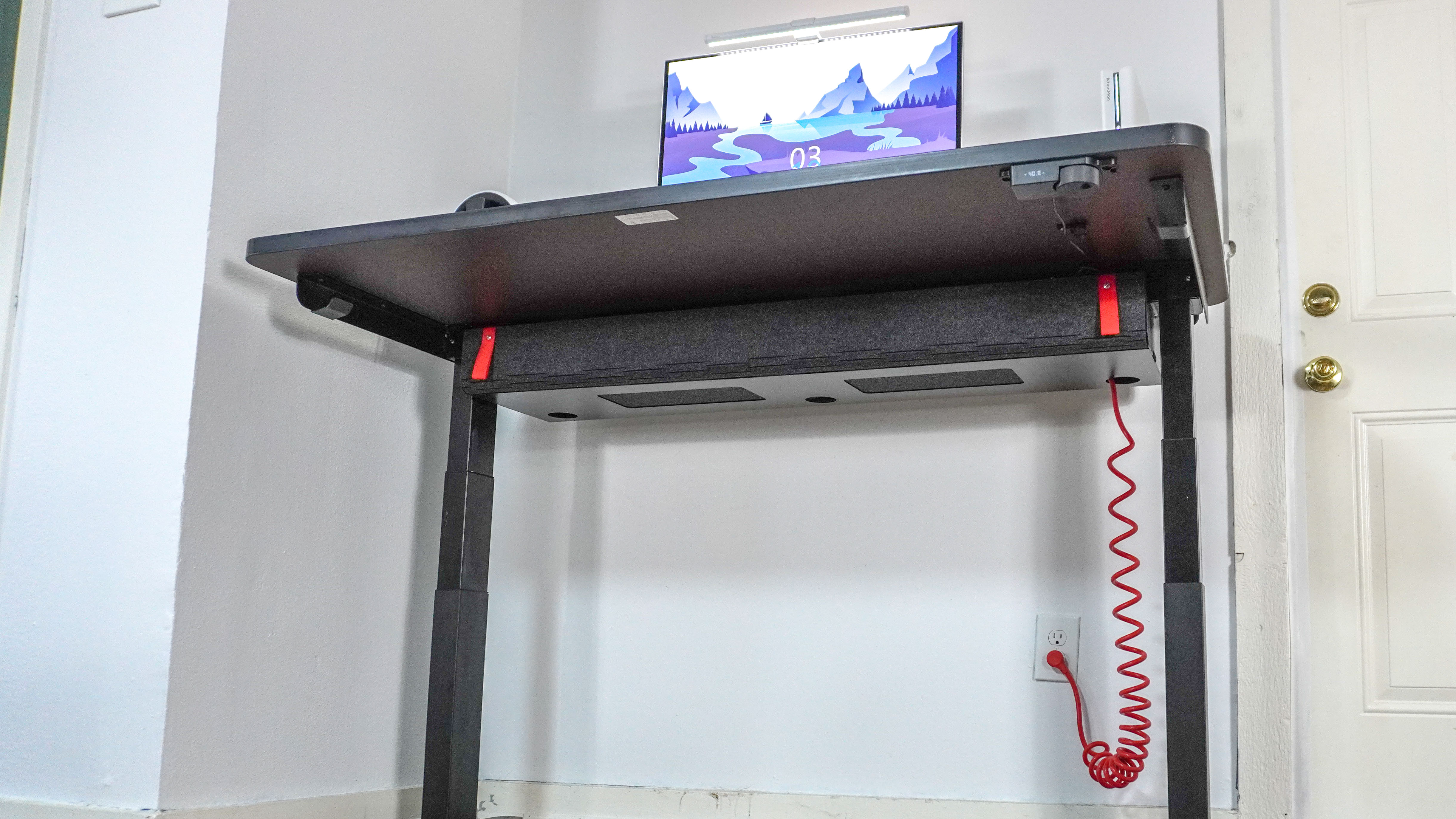 The Herman Miller Coyl Gaming Desk raised up showing off its red coiled cable and the red straps on its cable management tray