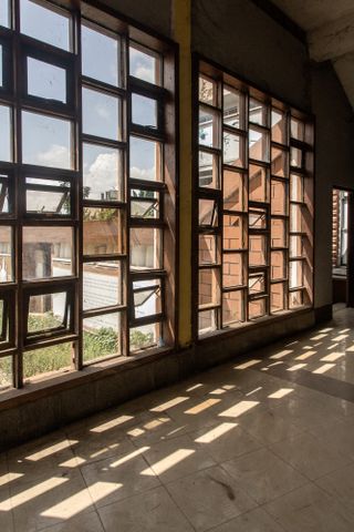 Interior image of the perforated wall at Oba Akenzua Cultural Centre in Benin City, surrounding garden area view through the glass, sunlight casting shadows on the stone tile floor, open doorway