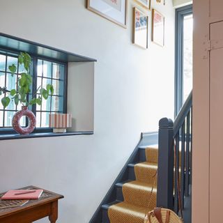 A white hallway with a staircase painted in blue with a jute runner rug on top