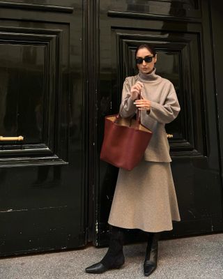 Influencer wears two-piece sweater set with knit midi skirt, black boots, and brown tote bag, standing on Paris street.