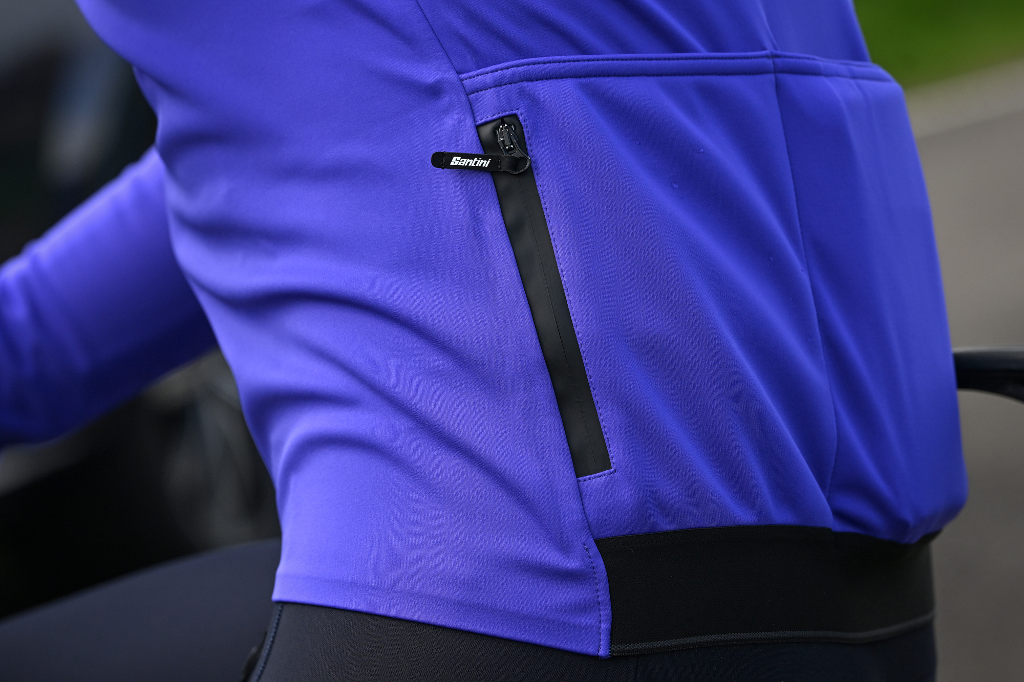 close up of the rear of a purple jacket showing the open pockets and the zipped security pocket